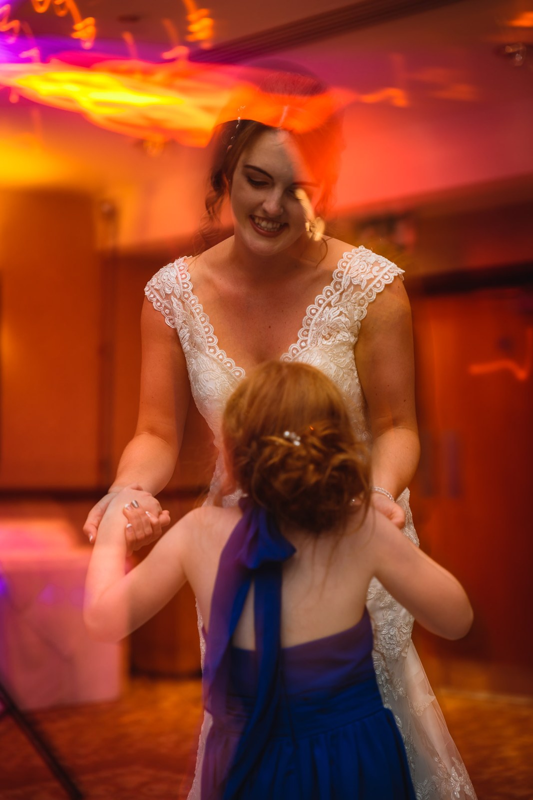 Bride dancing hand in hand with the flower girl in blue under warm lights