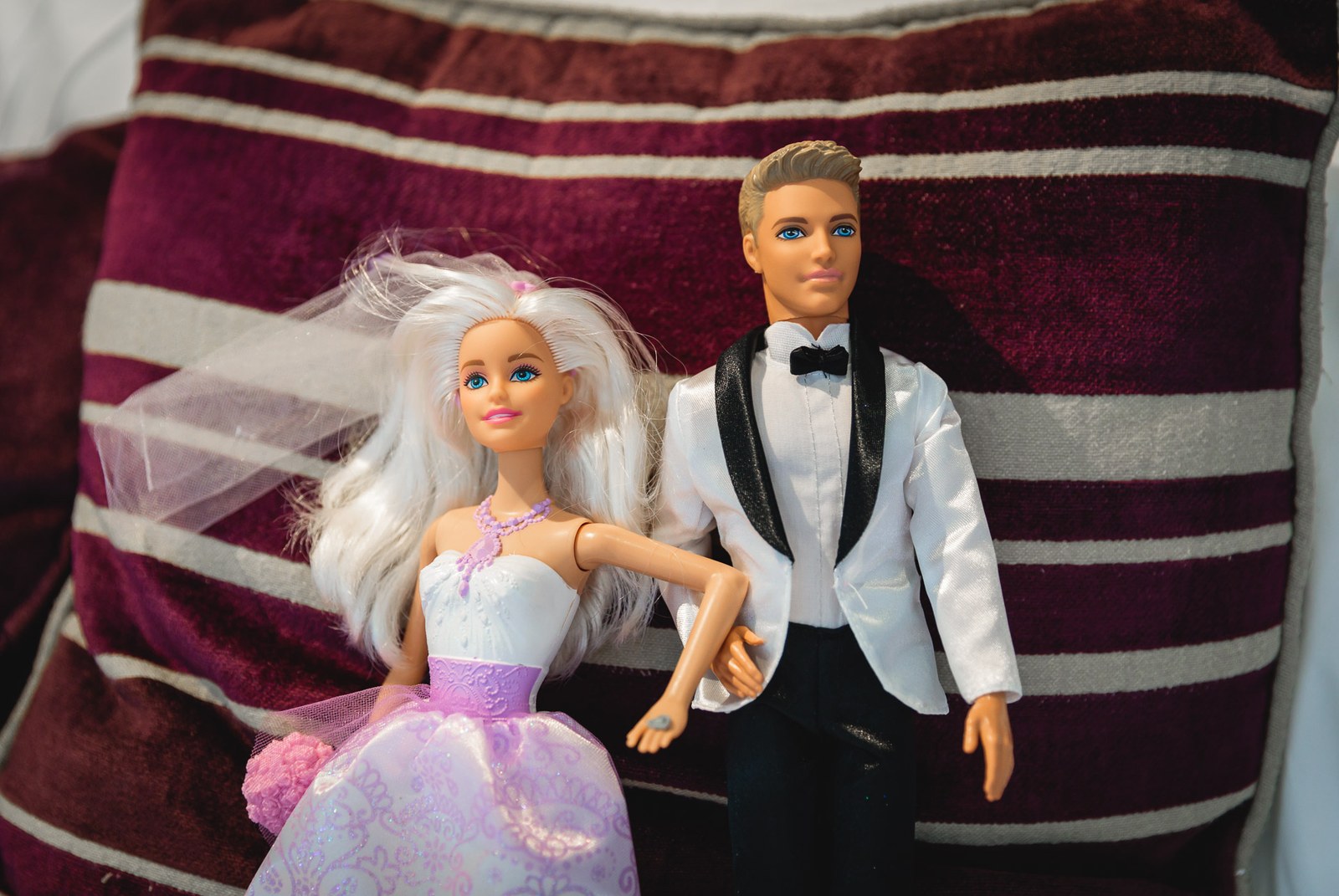 Bride and groom dolls dressed for a wedding propped on a striped cushion