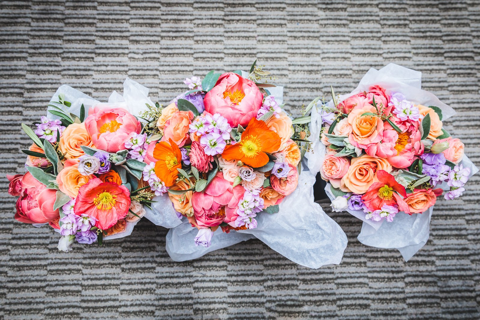 Three coral and peach bridal bouquets wrapped in tissue on a rug