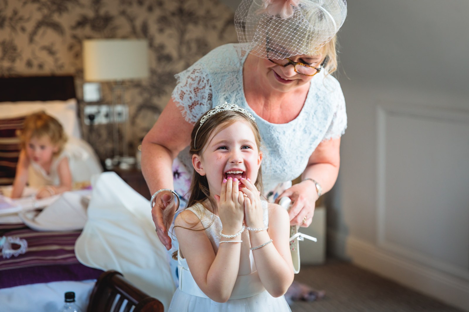 A laughing flower girl in a tiara being helped by an older female guest