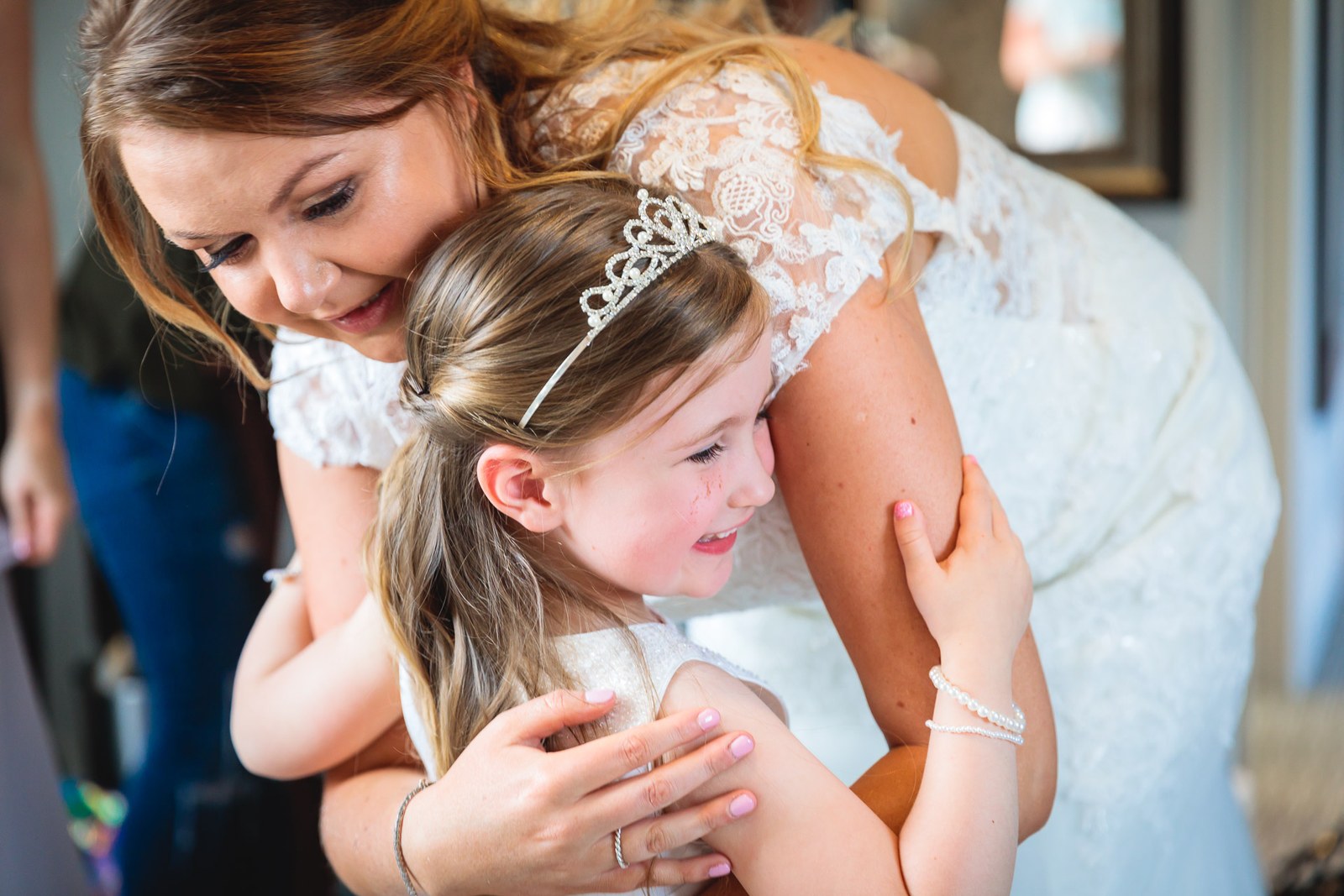 Bride embracing a flower girl in a tiara in the getting-ready room