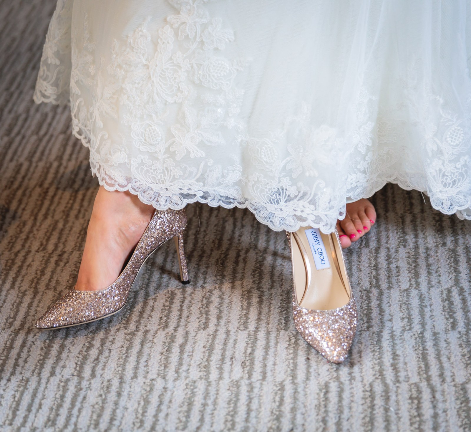 Close-up of the bride's glittering heels beneath the lace hem of her gown