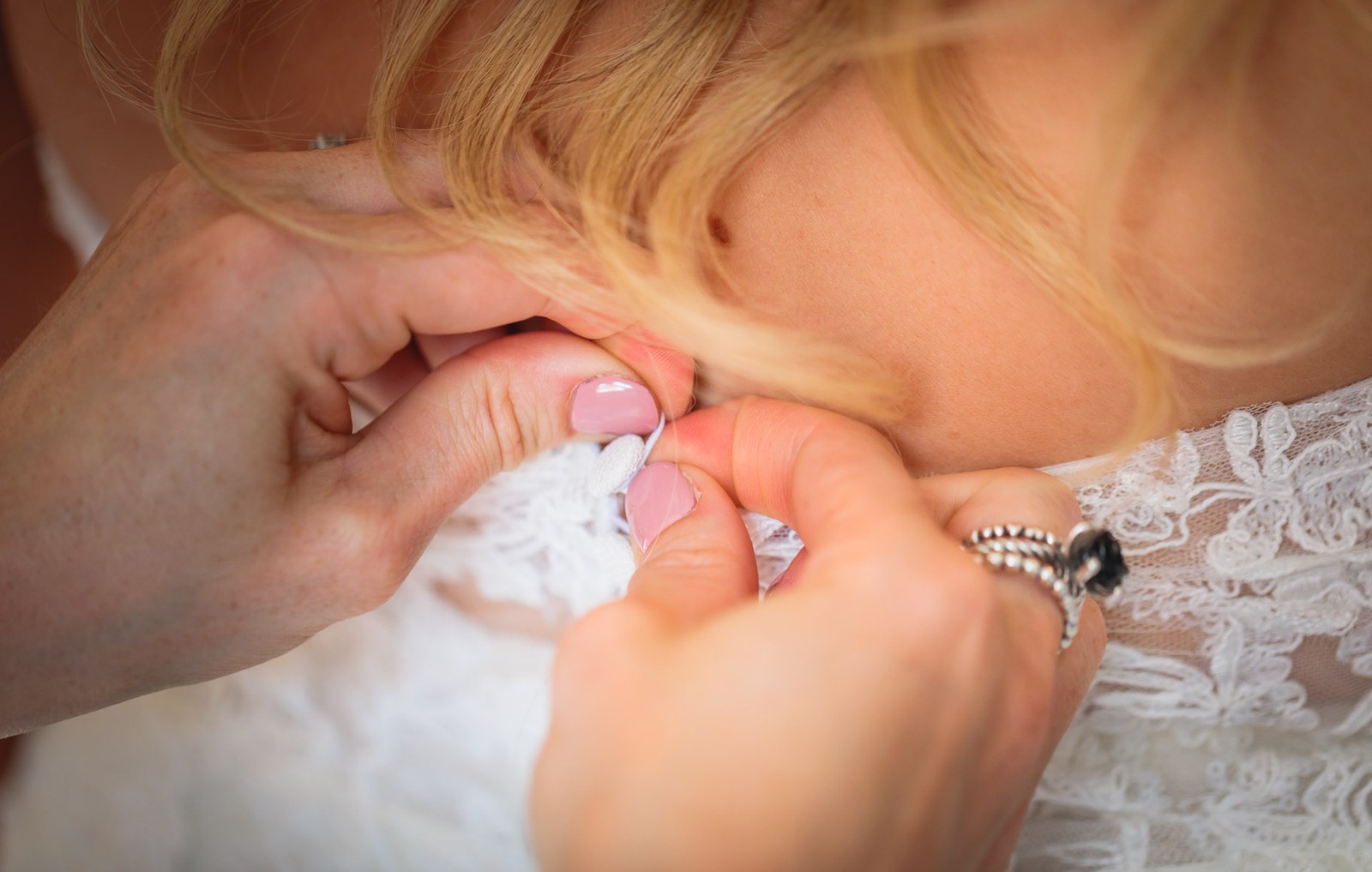 Hands fastening the buttons at the back of the bride's lace dress