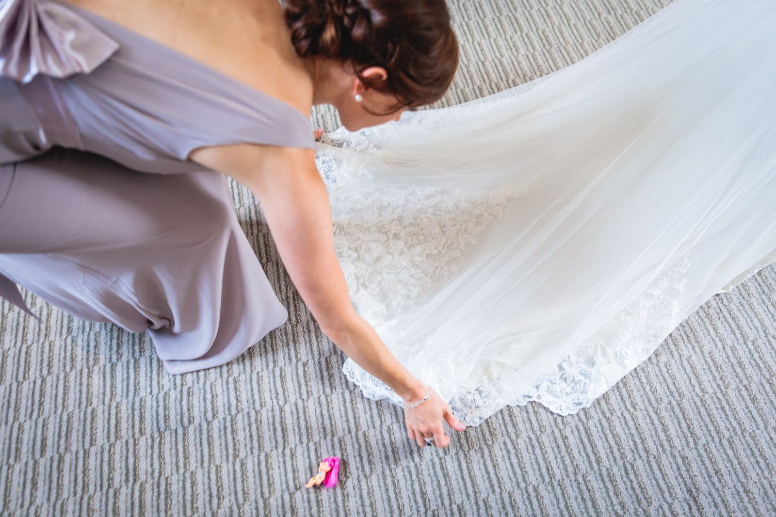 A bridesmaid kneeling to arrange the bride's veil and train on the floor