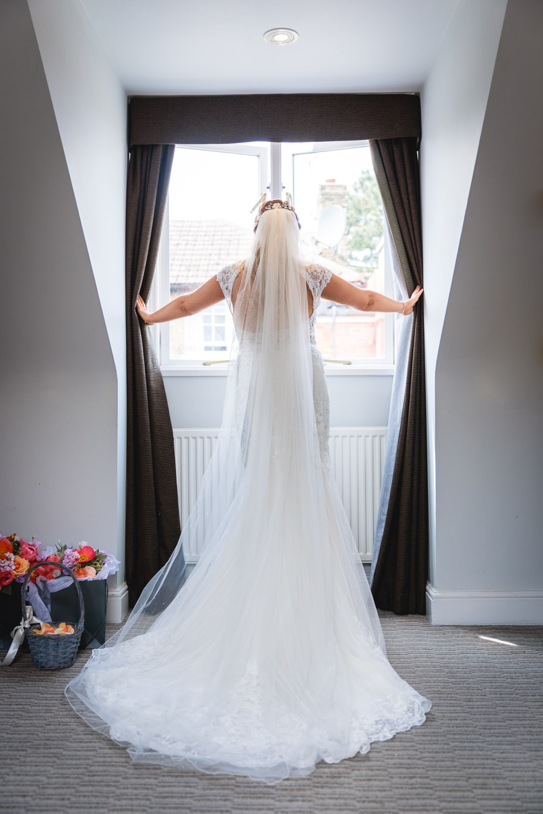 Bride from behind opening the curtains at a window, veil and train trailing