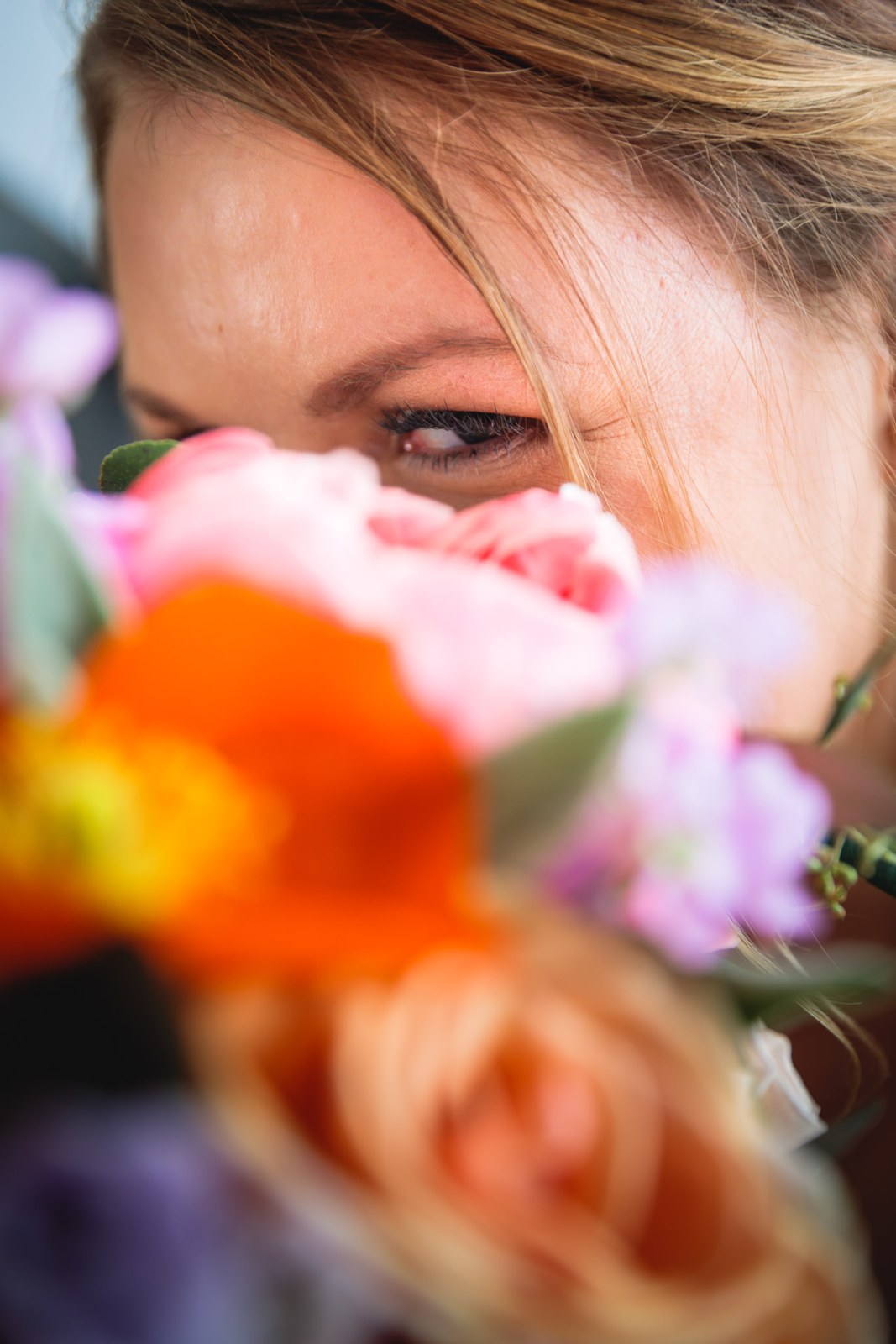 Close-up of the bride's eye peeking over her bright coral bouquet