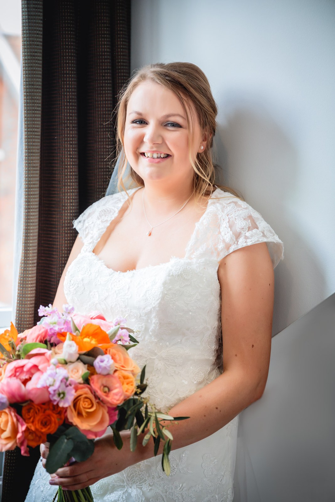 Bride in her lace gown holding a vivid coral and orange bouquet