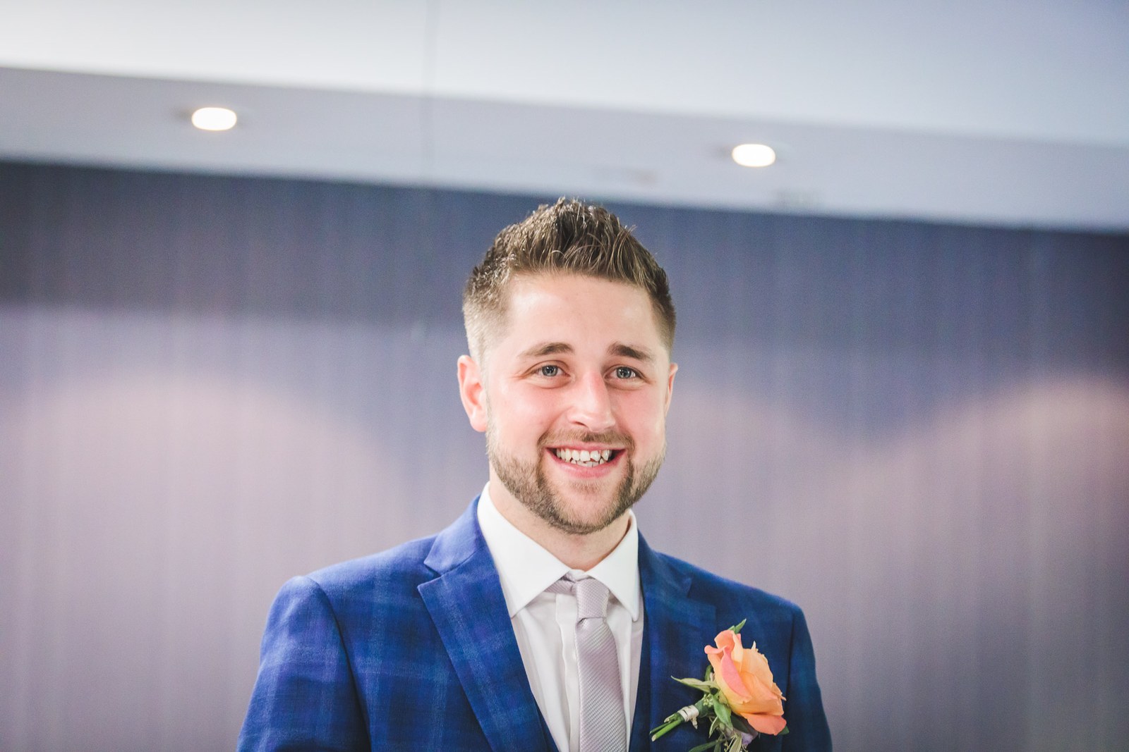 Groom in a checked blue suit smiling as he waits at the front of the ceremony