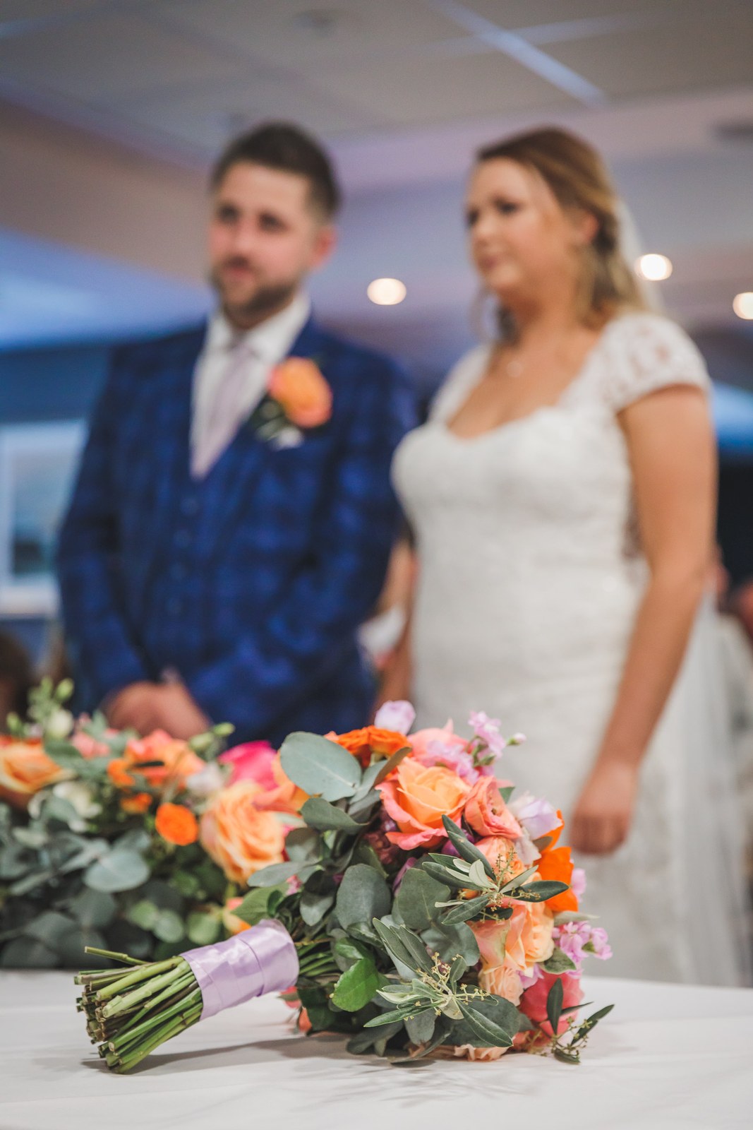 Bride and groom at the front of the ceremony, coral bouquet in the foreground
