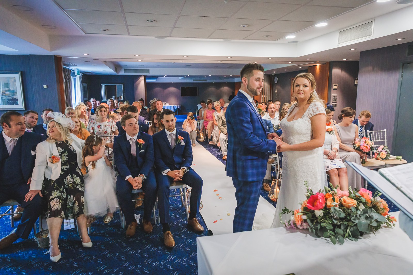 Wide view of the ceremony room with the couple at the front and guests seated