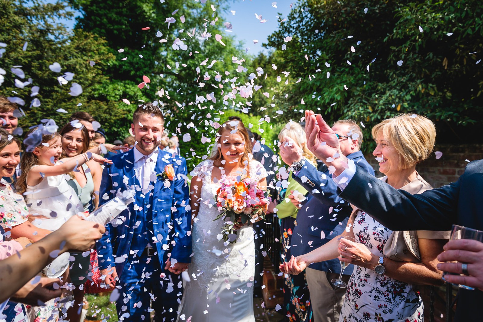 The newlyweds walking through a shower of confetti thrown by guests in the garden