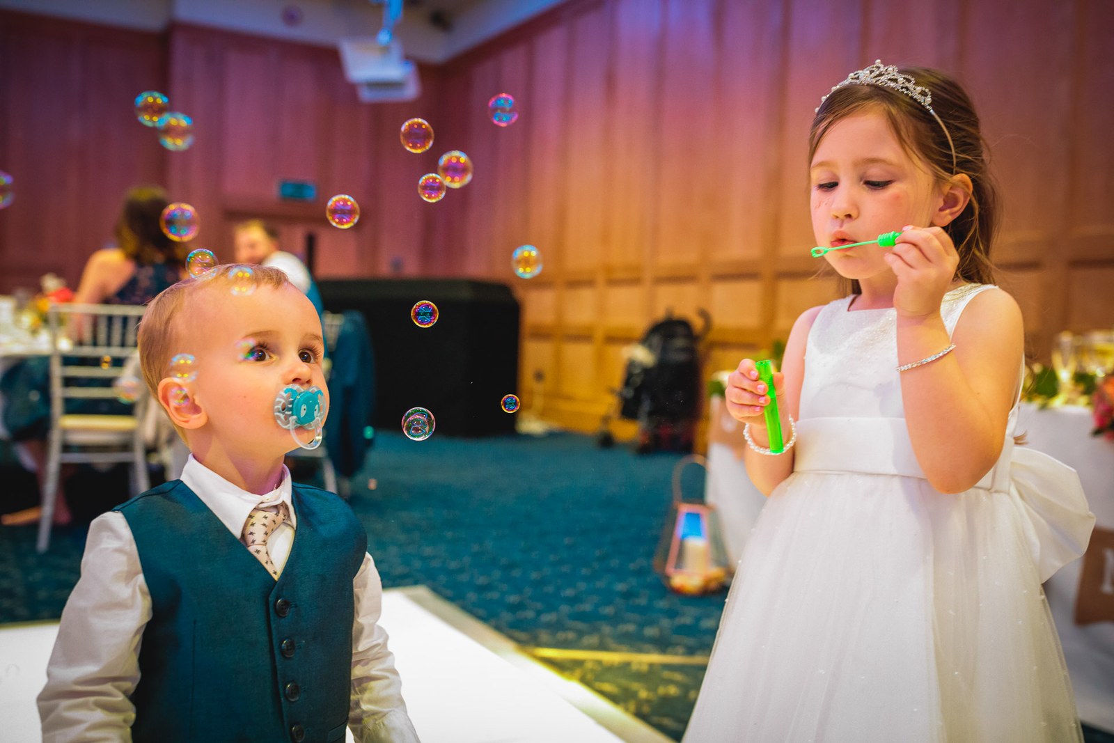 A page boy watching a flower girl blow bubbles in the reception