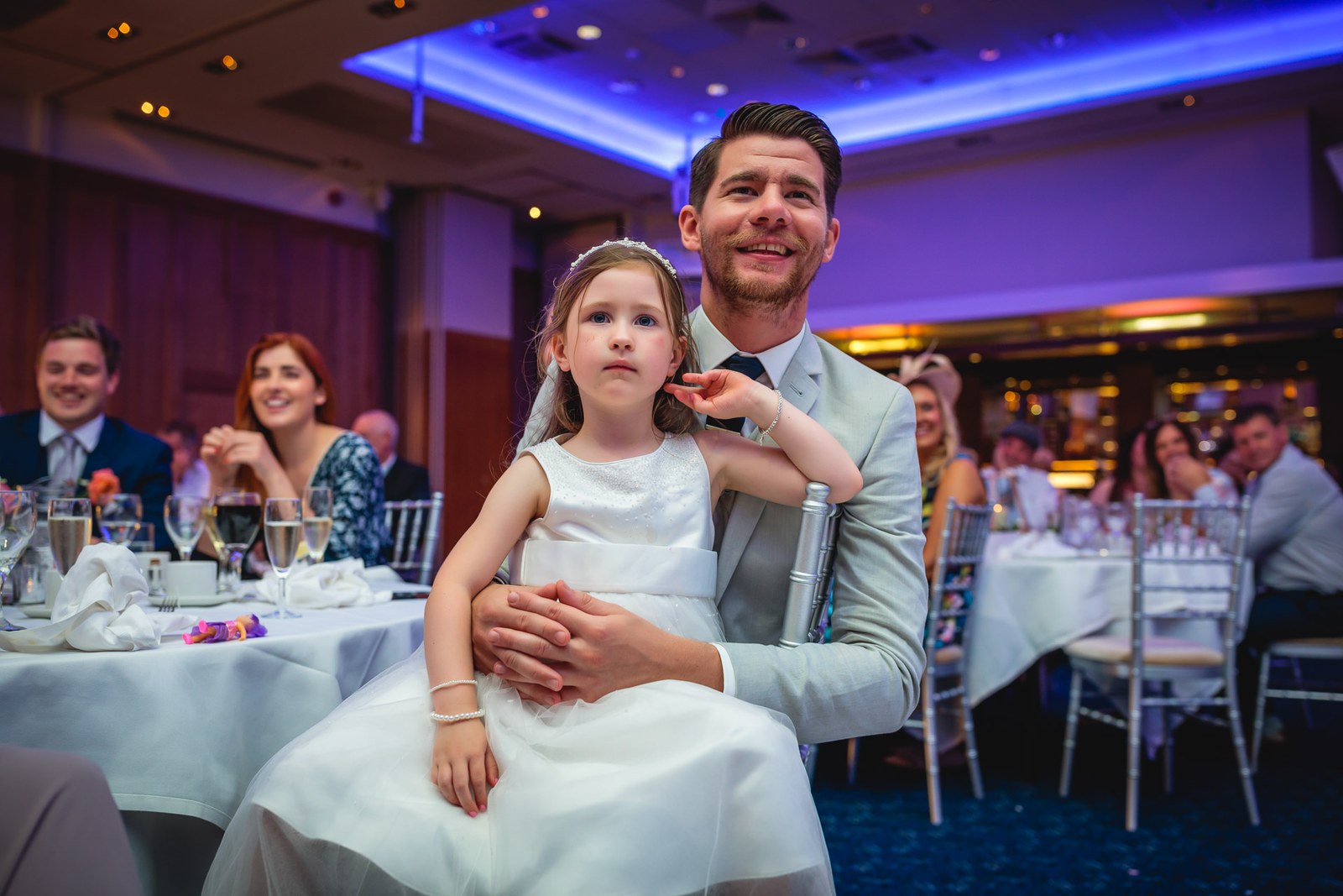 A guest in a grey suit holding a flower girl on his lap during the reception