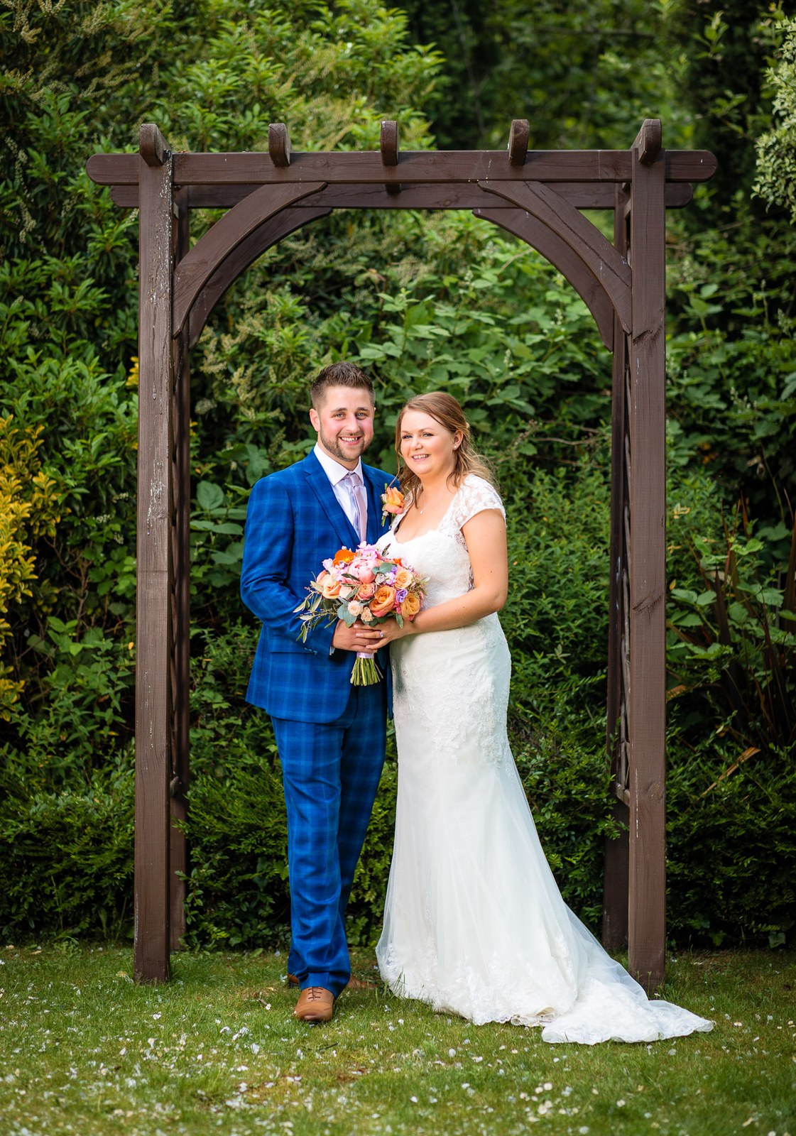 Bride and groom beneath a wooden garden arbour in the Mandolay Hotel grounds