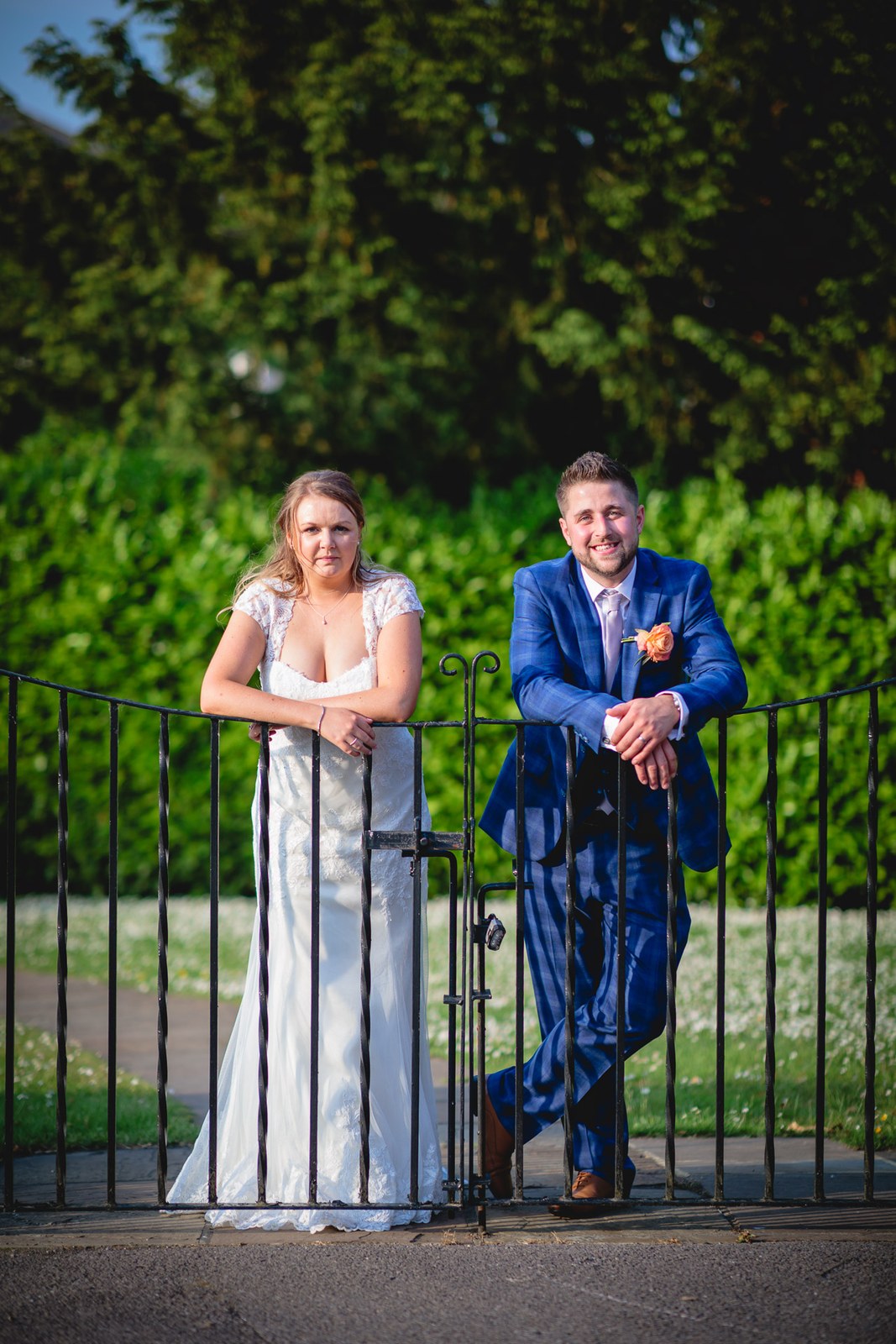 Bride and groom leaning on a wrought-iron garden gate in the grounds