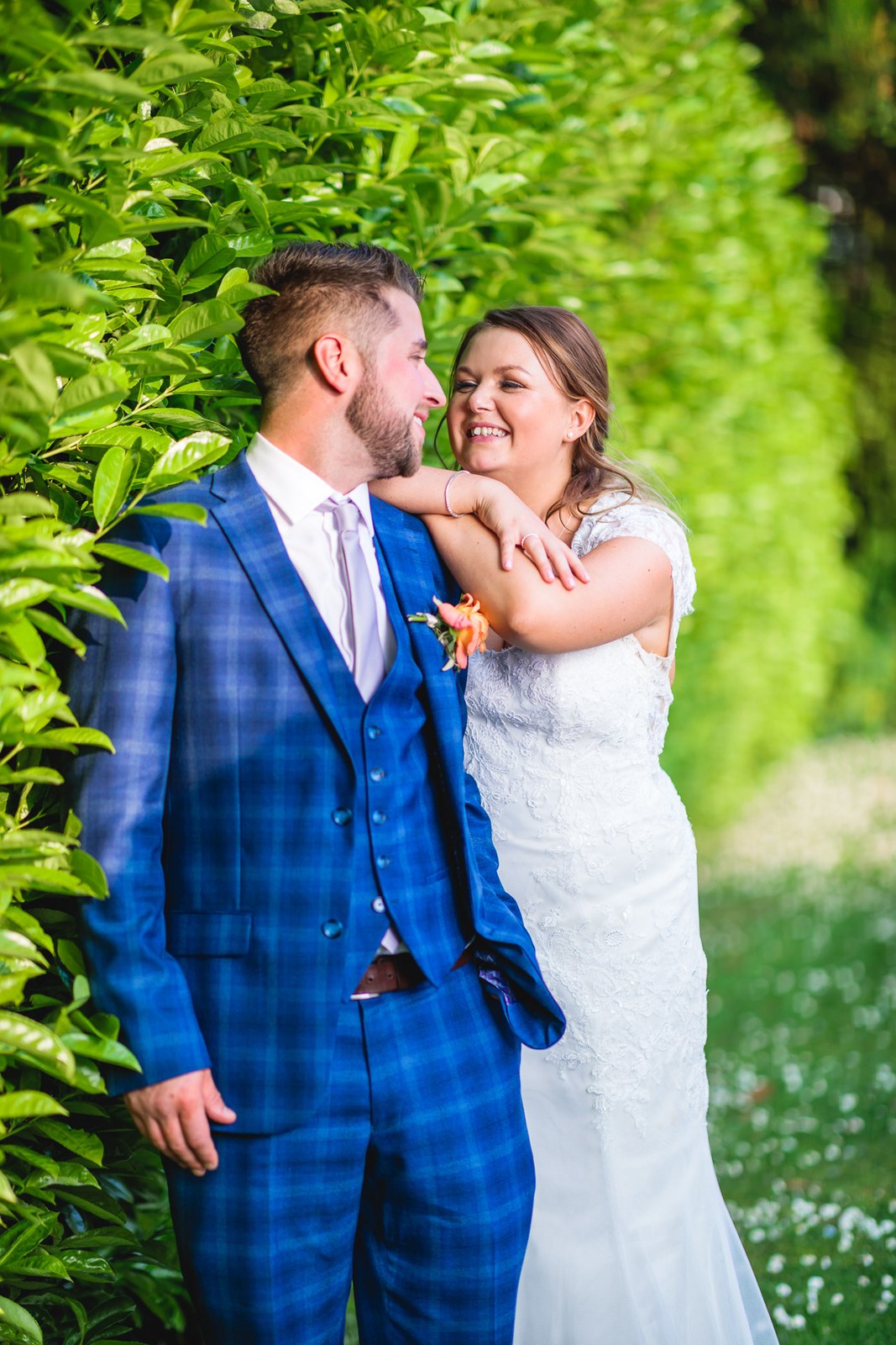 The couple by the garden hedge, the bride's arm resting on the groom's shoulder