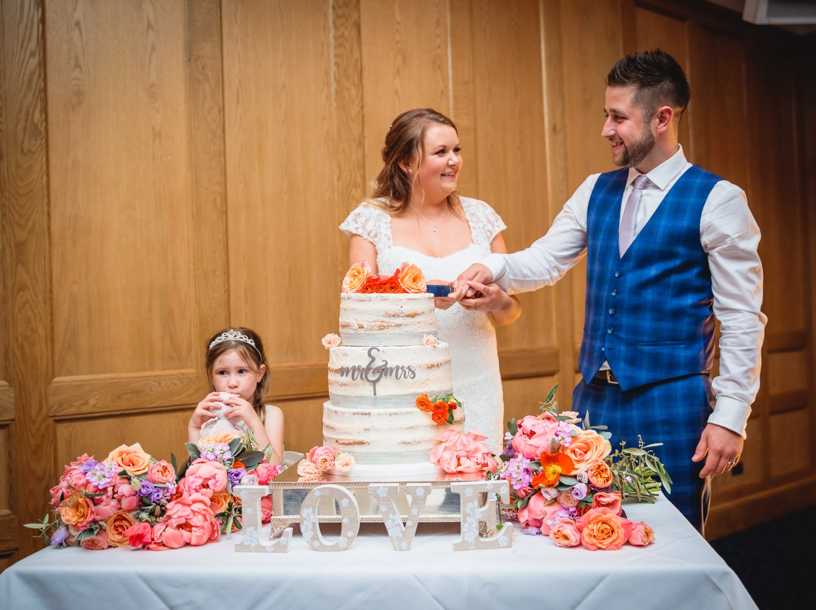 Bride and groom cutting their semi-naked cake beside LOVE letters and flowers