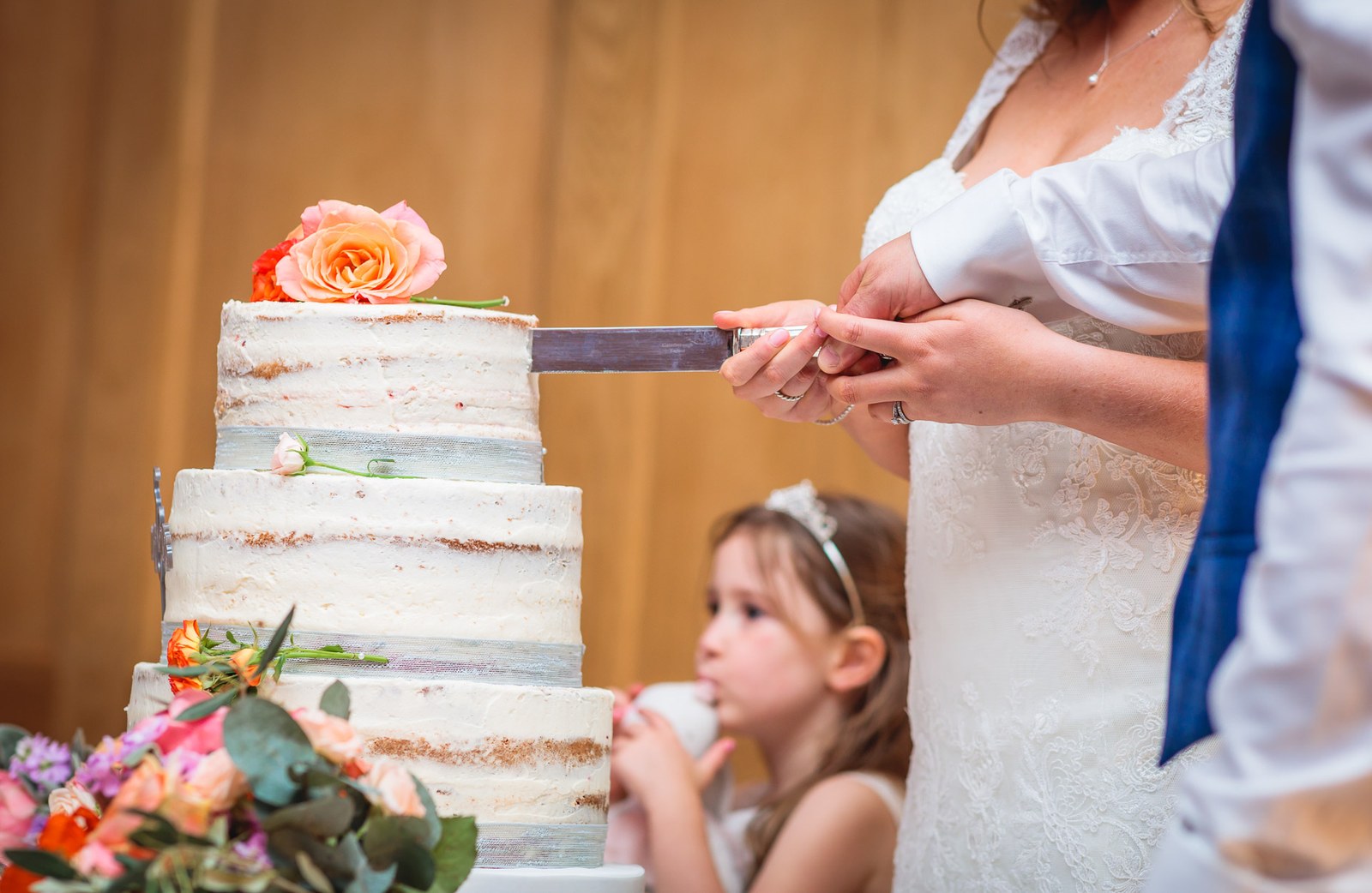 Close-up of the couple cutting the cake as a flower girl watches