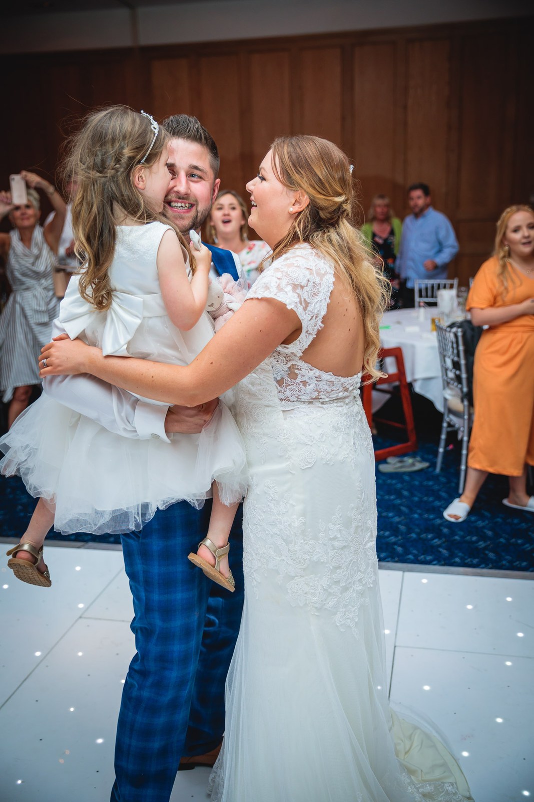 Bride and groom dancing with a flower girl in their arms on the floor