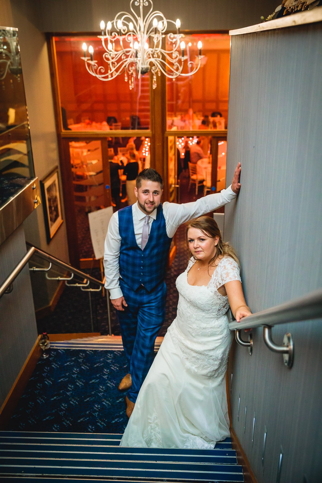 Bride and groom on the Mandolay Hotel staircase beneath a crystal chandelier