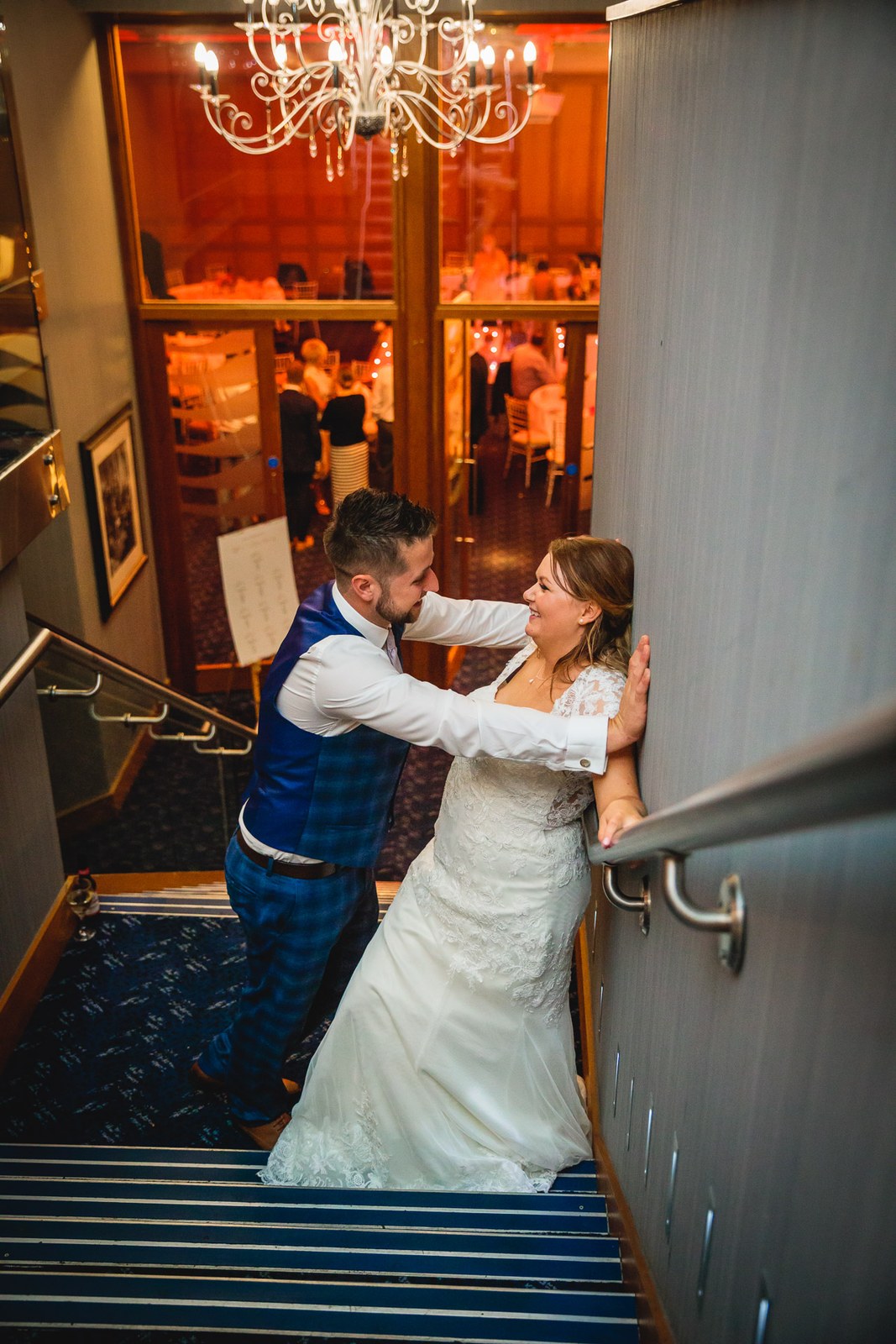 The couple embracing on the hotel staircase under the chandelier