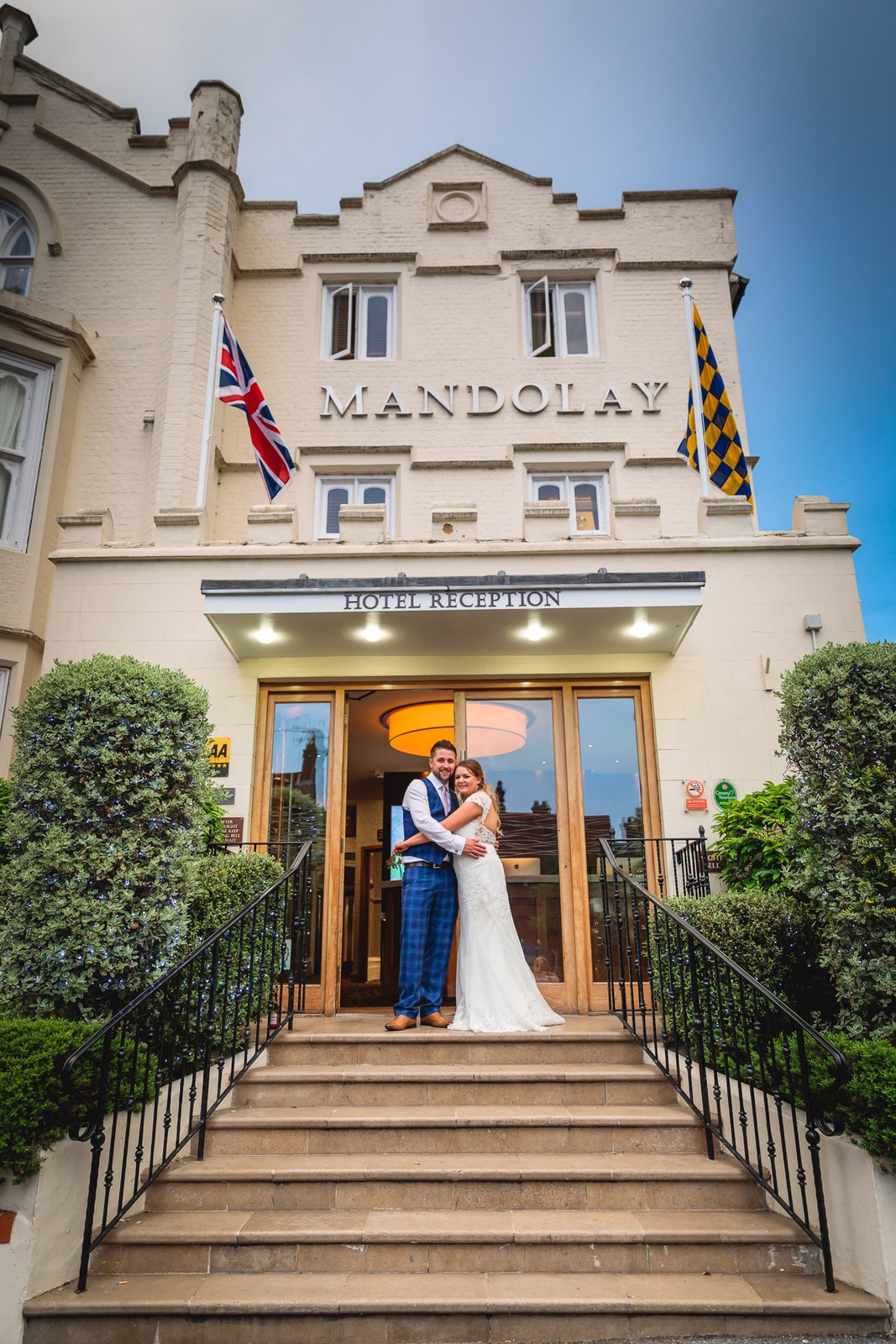 Bride and groom embracing in the lit entrance of the Mandolay Hotel at the top of the steps