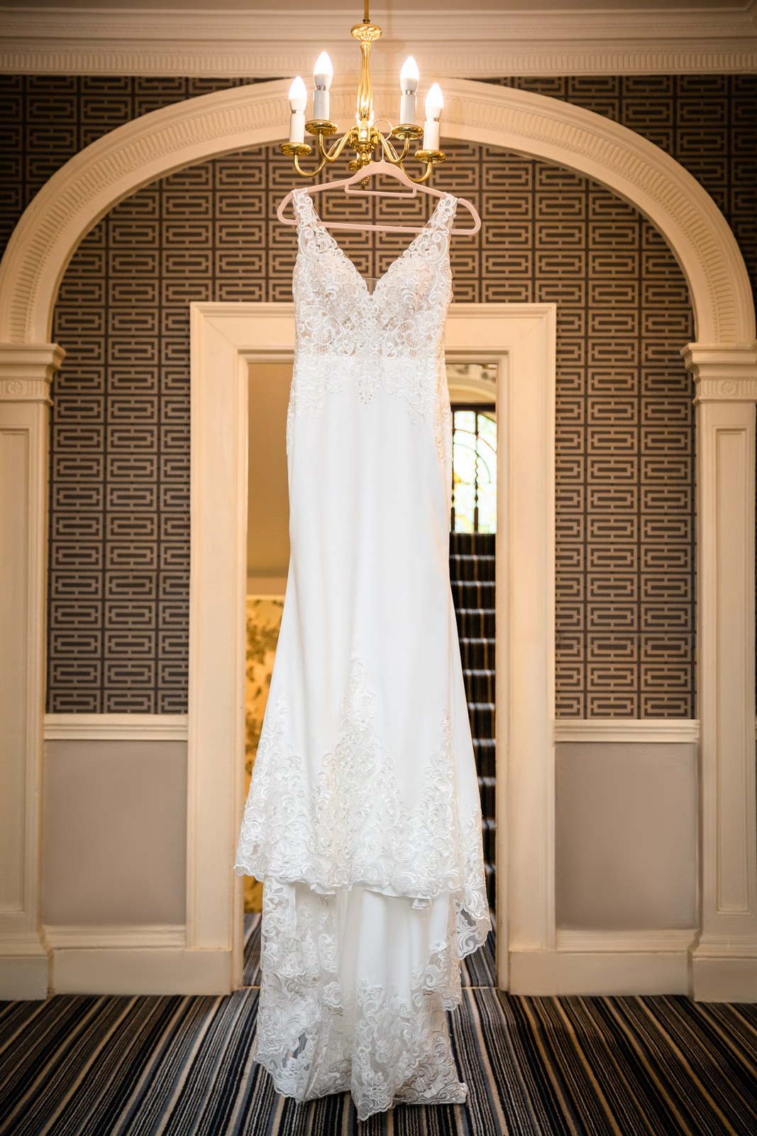 Lace wedding dress on a hanger in an arched doorway of Moore Place Hotel beneath a chandelier