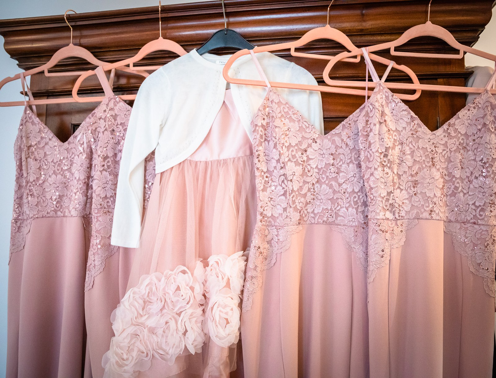 Dusky-pink lace bridesmaid dresses hanging on a wardrobe