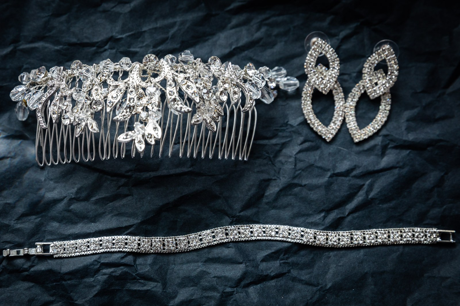 Close-up of a crystal hair comb, diamante earrings and bracelet on dark paper