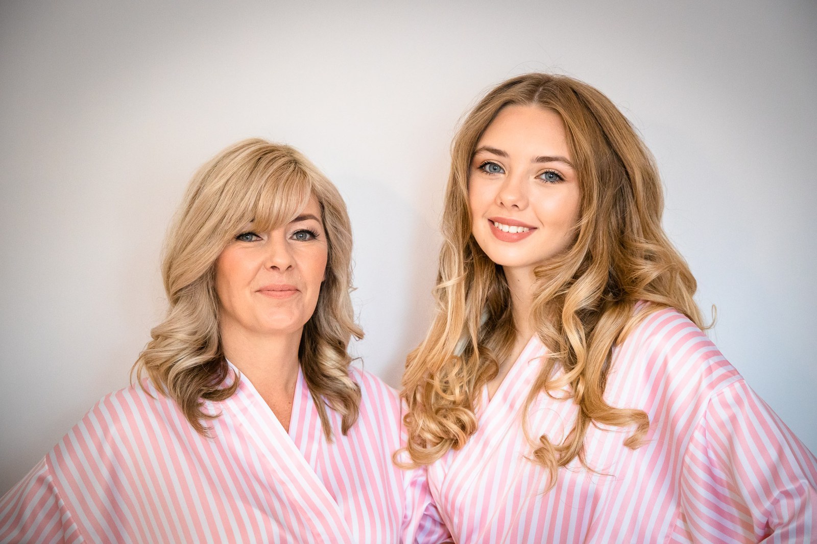 Two bridesmaids in pink striped robes posing against a plain wall