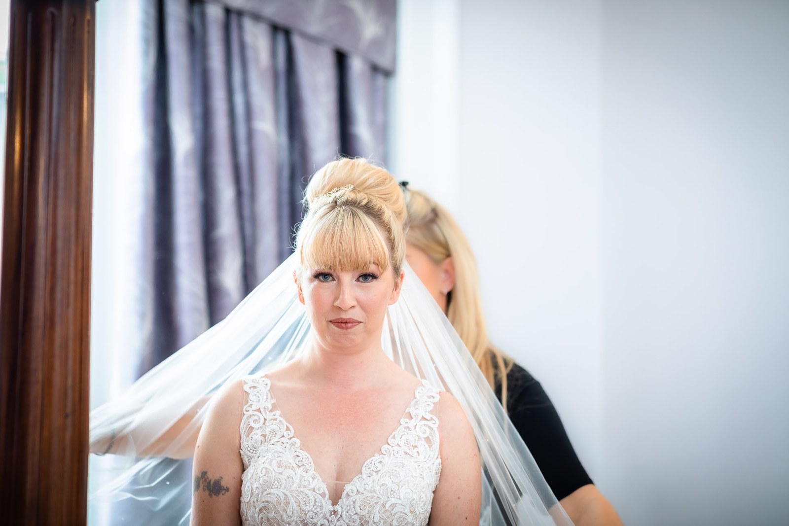 Bride looking to camera as she finishes getting ready in her gown and veil