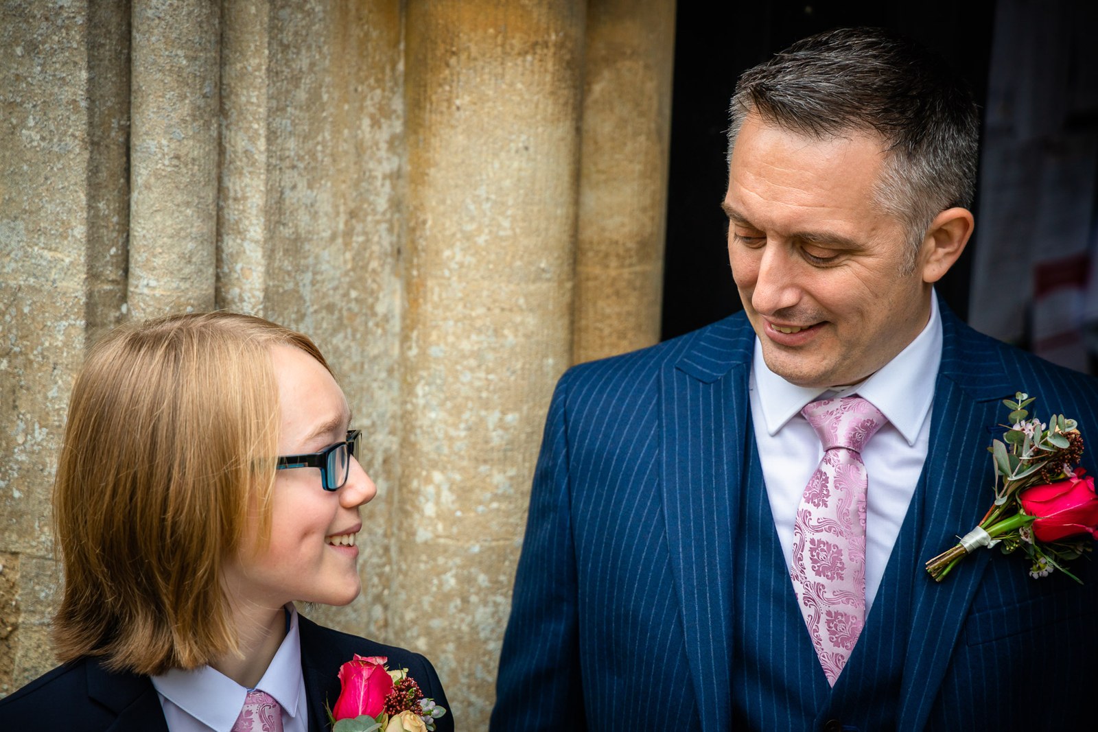 A young usher in a suit beside an older man in the stone church porch