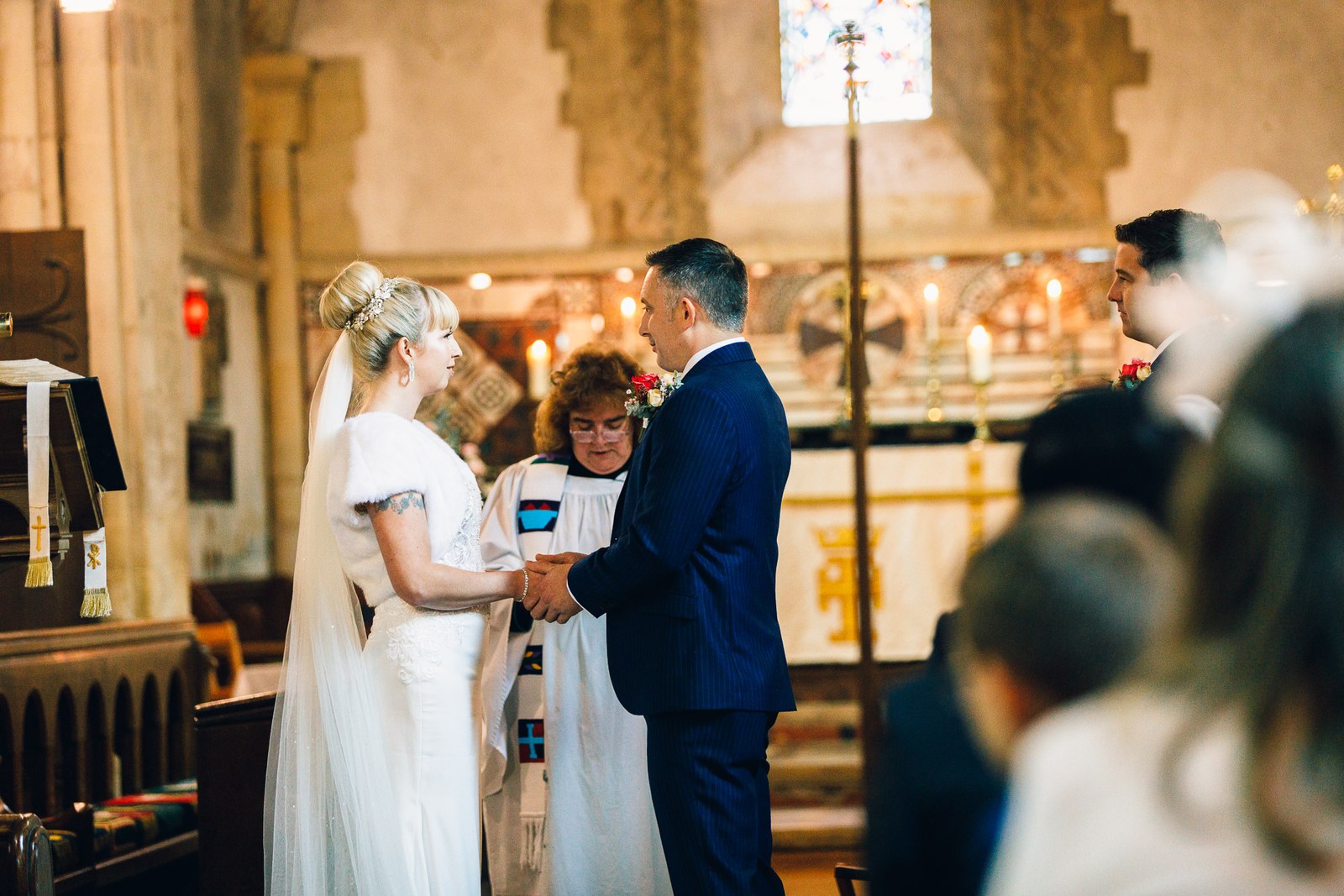 Bride and groom exchanging vows with the vicar in the candlelit church
