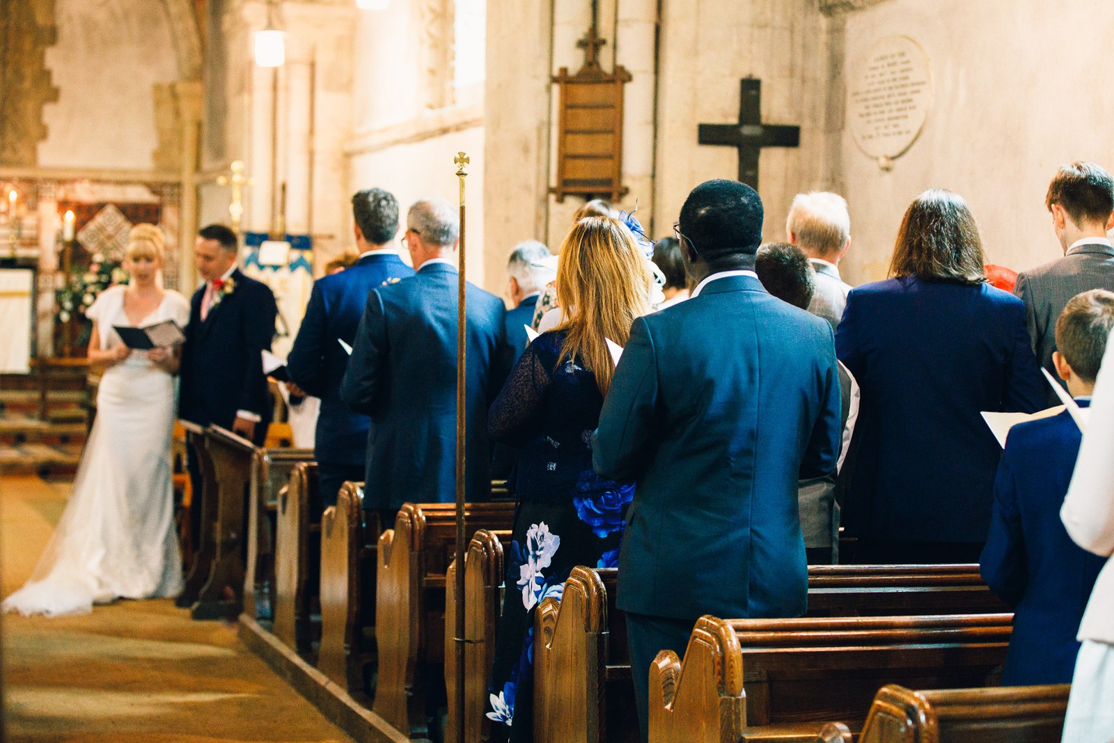 The couple standing during the ceremony, guests in the pews either side