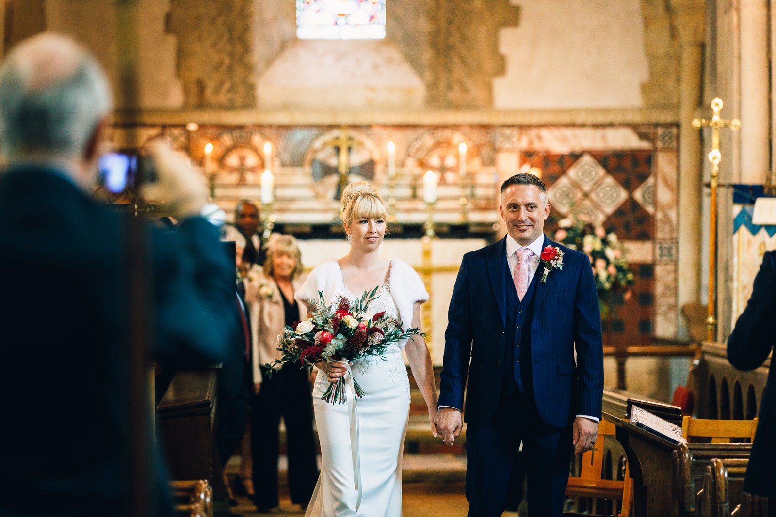 The newlyweds walking back down the aisle as a guest films on a phone