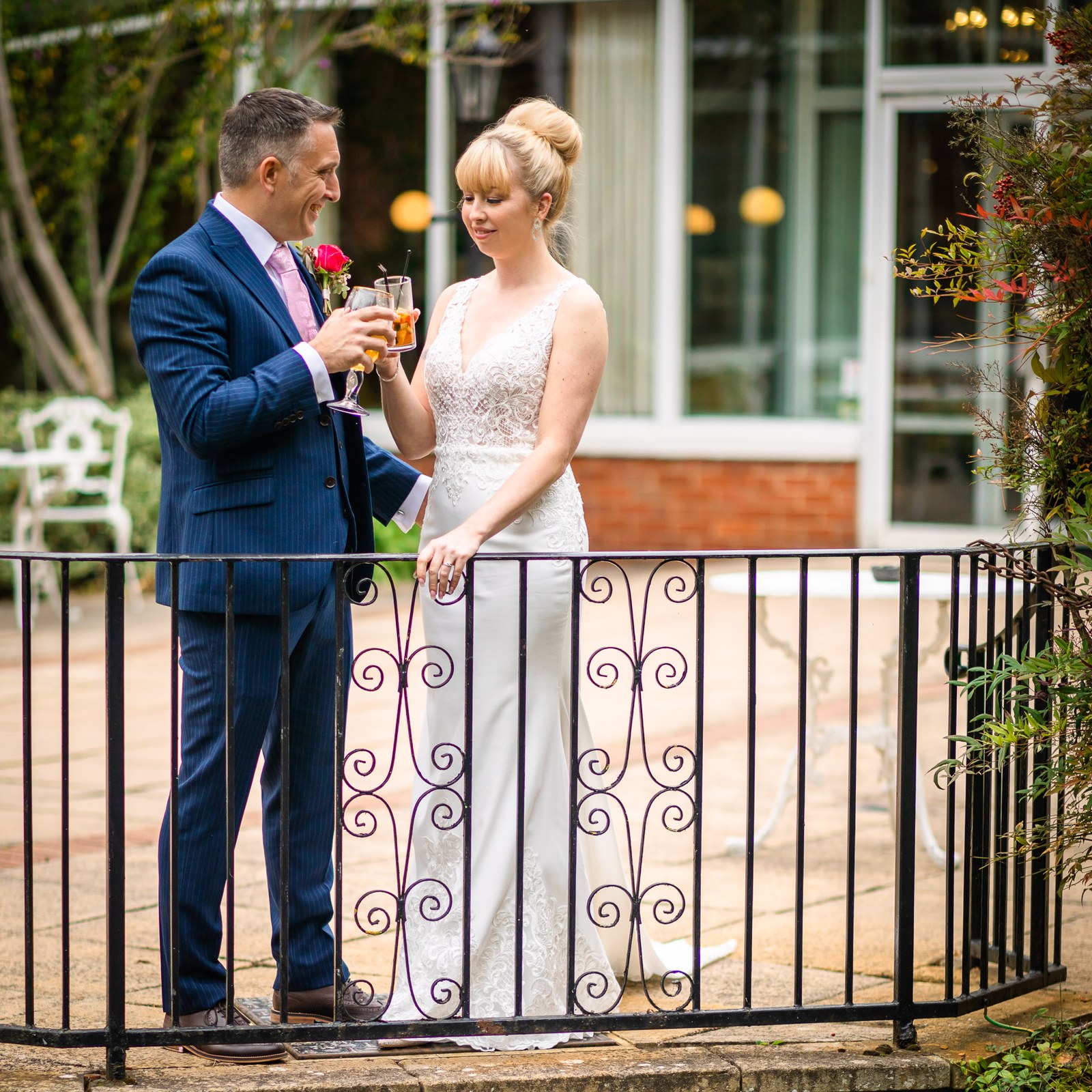 Bride and groom toasting with drinks at a wrought-iron railing on the hotel terrace