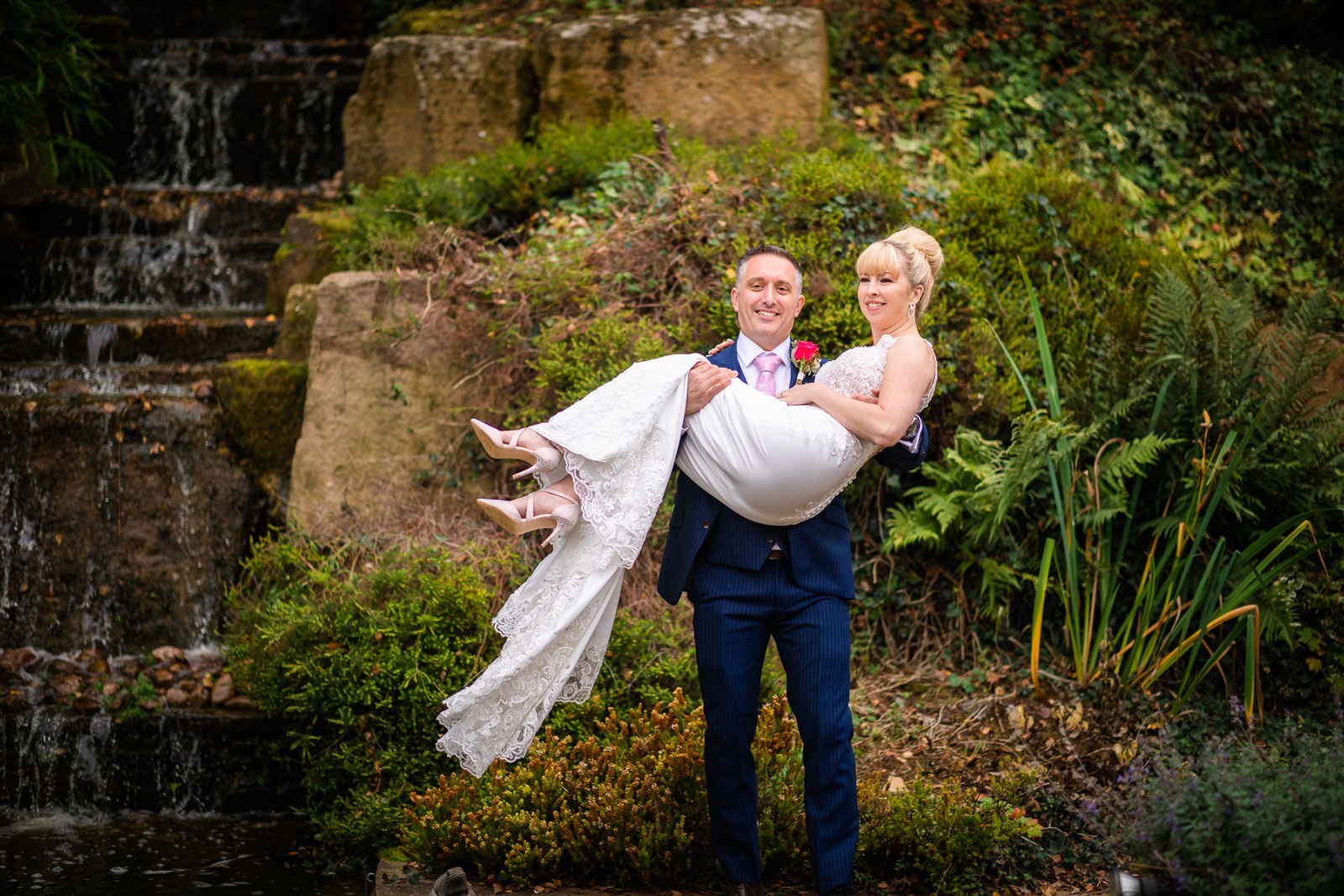 Groom carrying the bride in his arms before the hotel's rockery waterfall