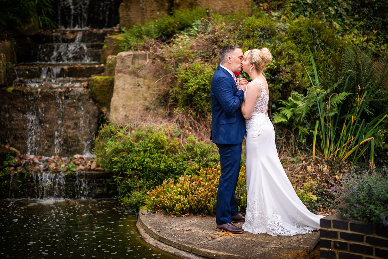 Bride and groom kissing beside the rockery waterfall and pond in the grounds