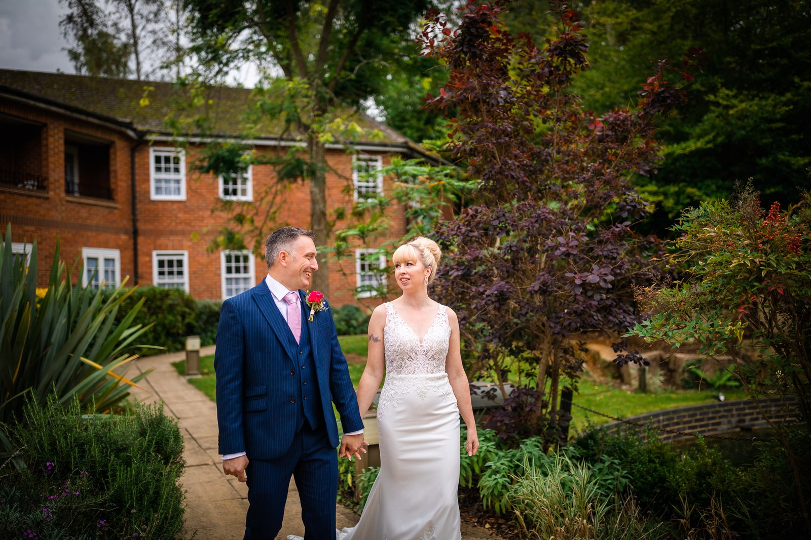 Bride and groom walking through the gardens with the red-brick hotel behind