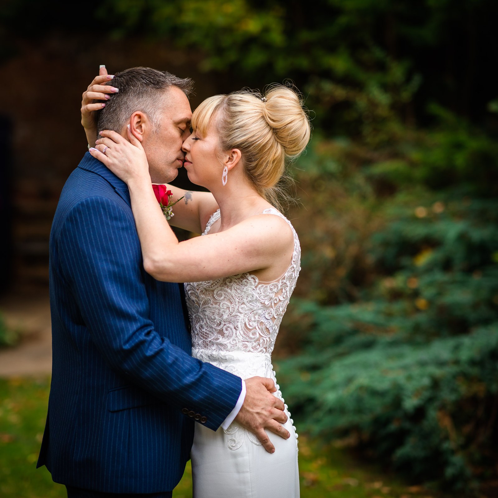 Bride and groom kissing in the grounds, her hand resting on his head