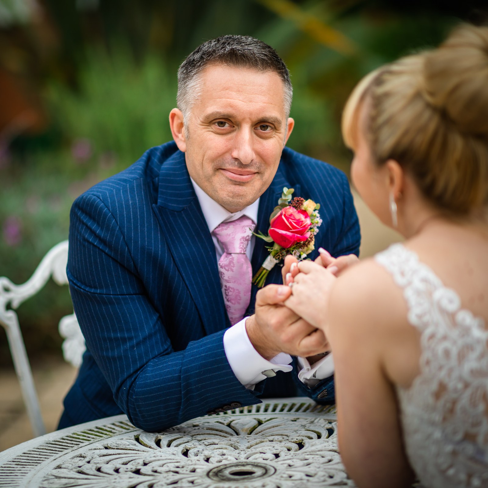 Close-up of the groom holding the bride's hands across a white garden table
