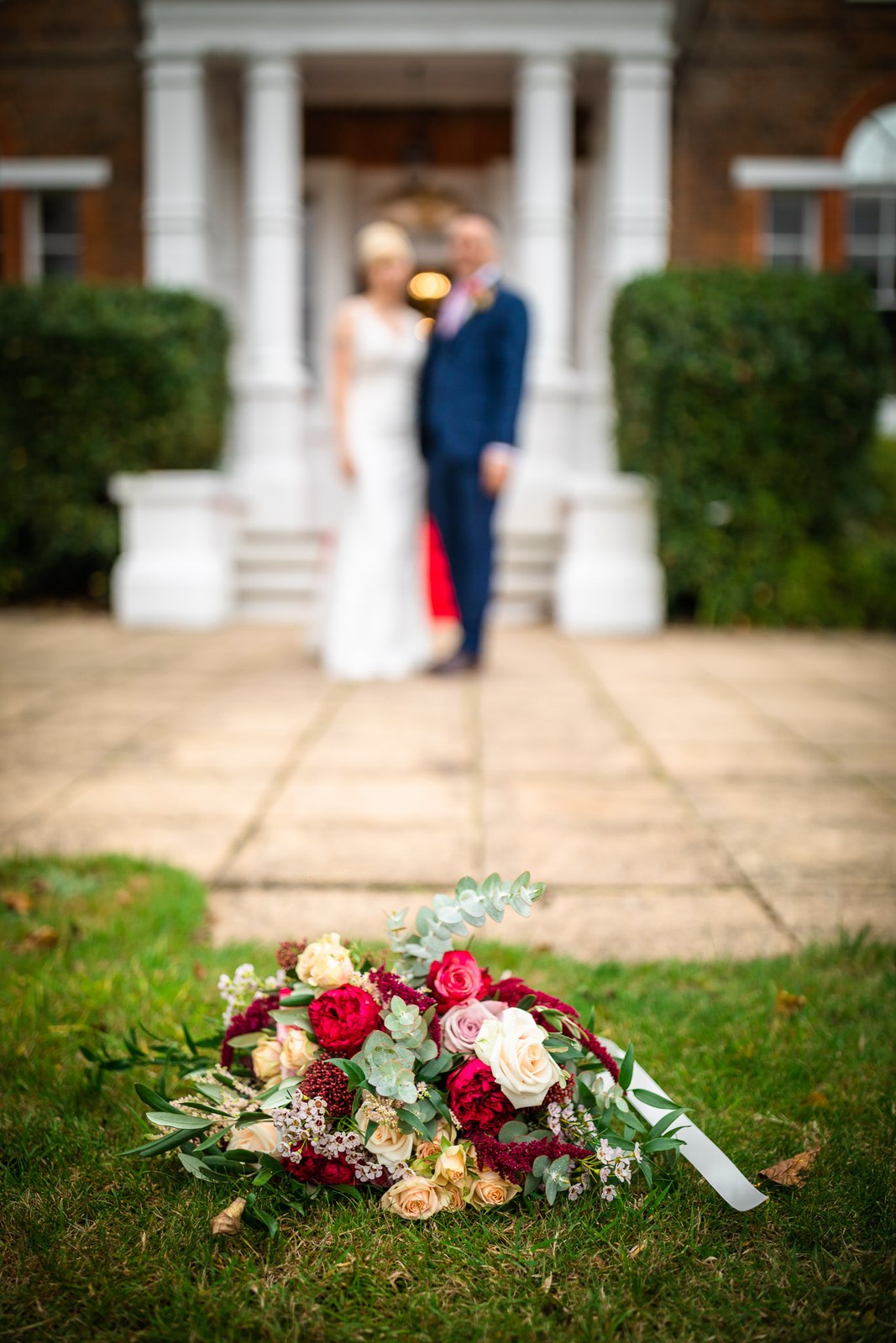The couple by the white columned portico, a bouquet resting on the lawn
