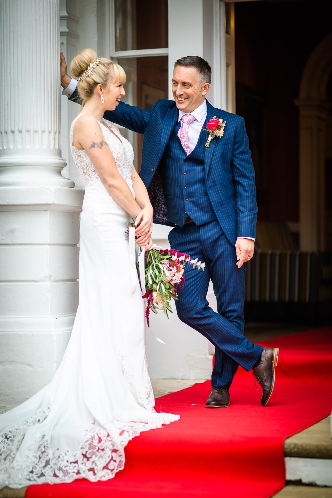 Bride and groom on the red carpet at the hotel entrance, groom against a pillar