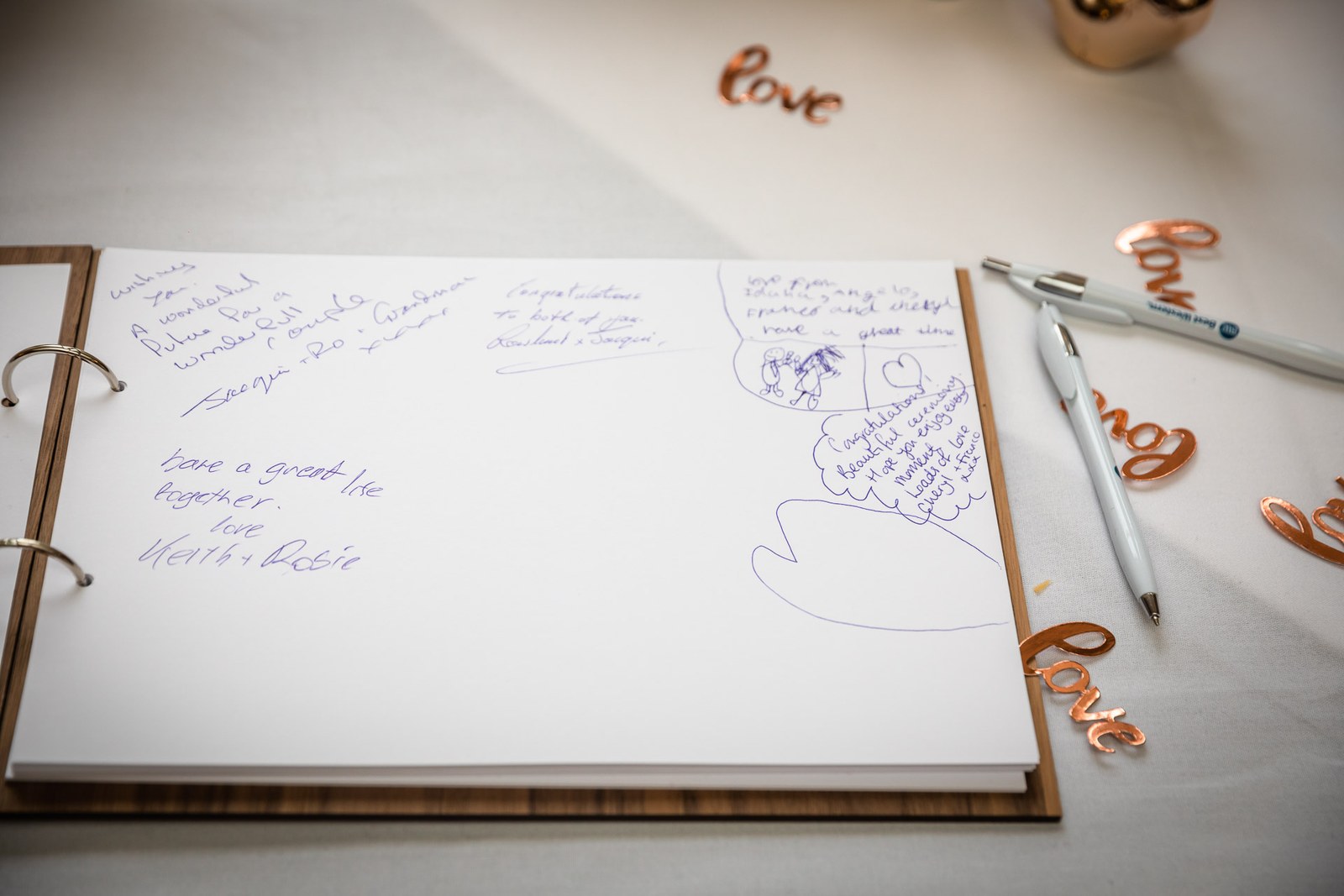 An open guest book with wooden love letters and a pen
