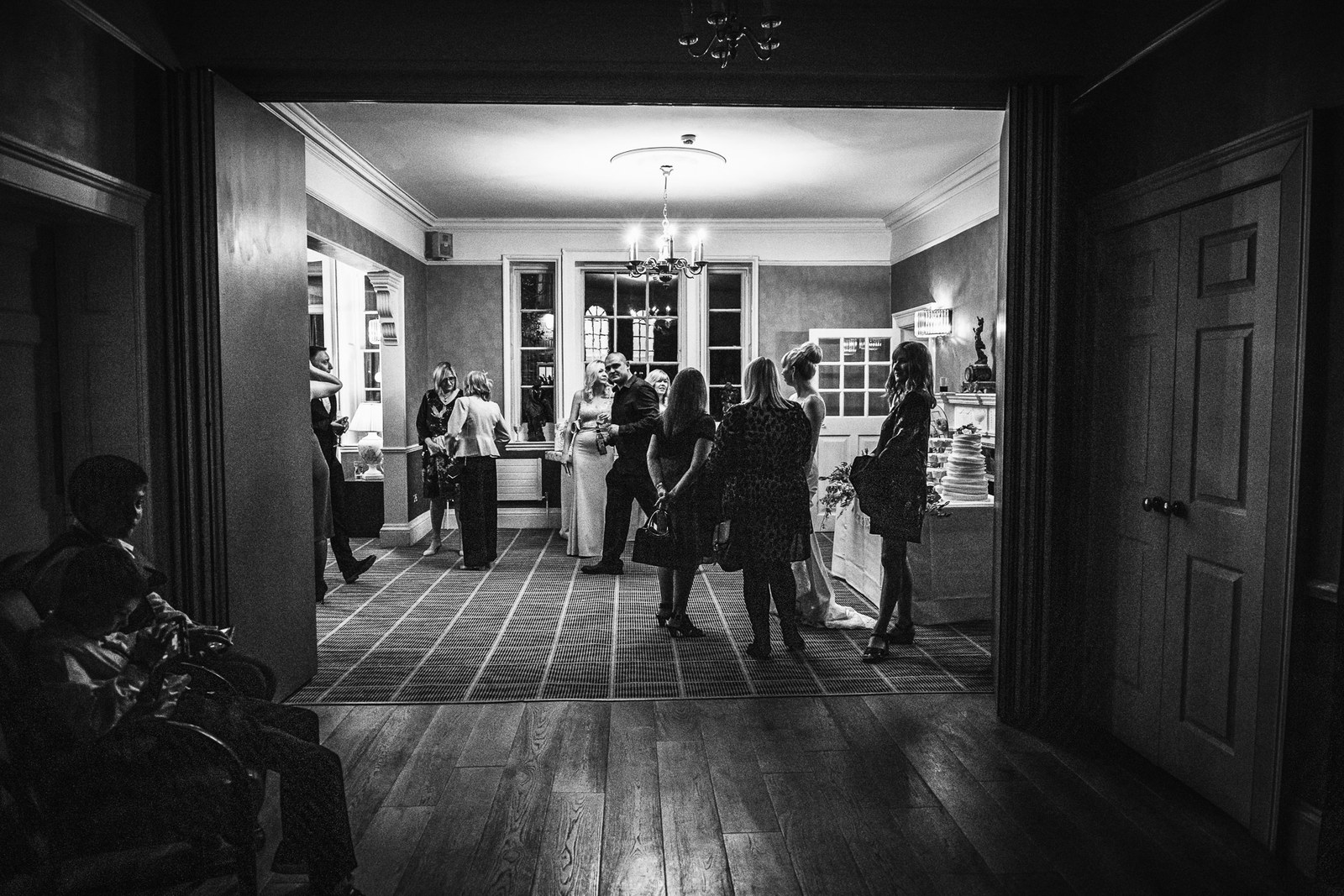 Black and white down a hotel corridor to guests gathered in a lit room