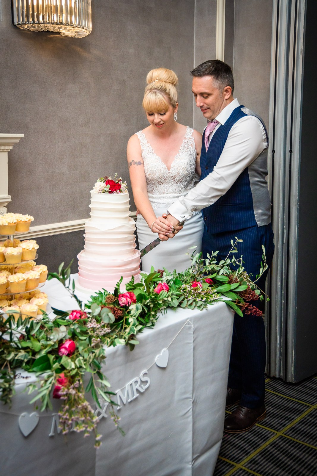 Bride and groom cutting their tiered cake dressed with flowers and a Mr and Mrs drape