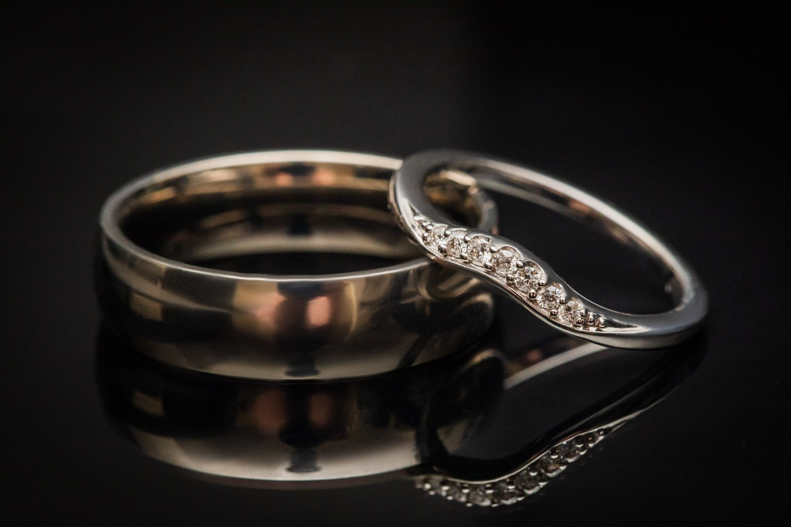Close-up of two wedding rings, one diamond-set, on a dark surface