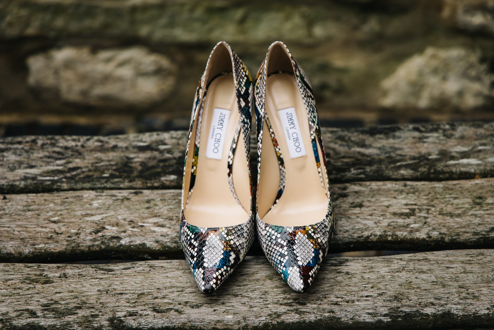 A pair of snakeskin-print heels resting on weathered wood