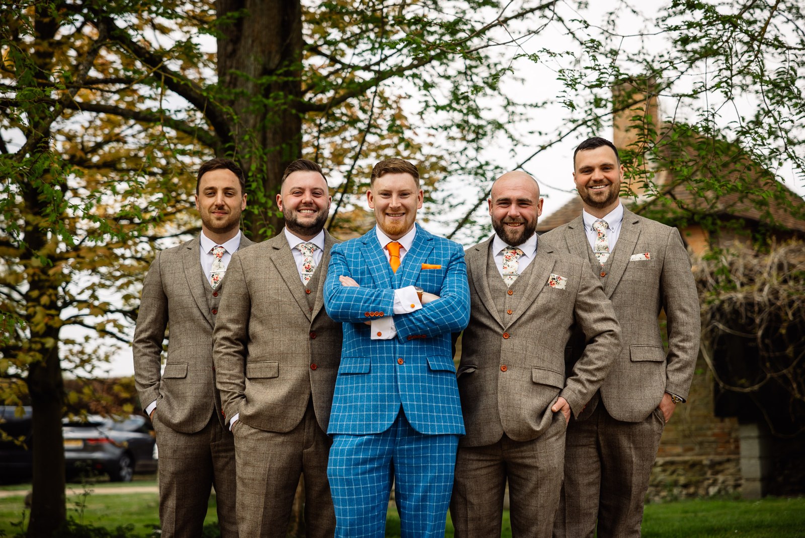 Groom in a bright blue check suit with groomsmen in tan tweed on the lawn
