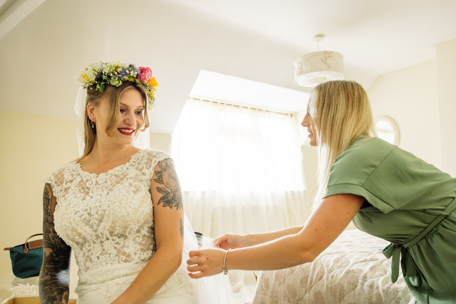 A helper smoothing the bride's veil and dress, the bride in her wildflower crown